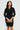 Woman wearing a black dress holding a clutch against a plain background