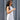 Woman in a white dress walking past a gray corrugated metal wall.