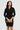 Woman wearing a black dress holding a clutch against a plain background